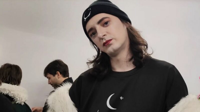 Proful trans de la Universitatea București s-a demachiat și a sărit la gâtul lui Bolojan. Anterior a avut apariții delirante, purtând coarne și ruj negru