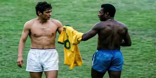 Mircea Lucescu și Pelé surprinși pe teren, la finalul unui meci de la 1970 FIFA World Cup, în timp ce fac schimb de tricouri. Pelé ține în mână tricoul galben cu numărul 10 al Braziliei, oferindu-l lui Lucescu, într-un moment simbolic de respect și fair-play între cei doi jucători.